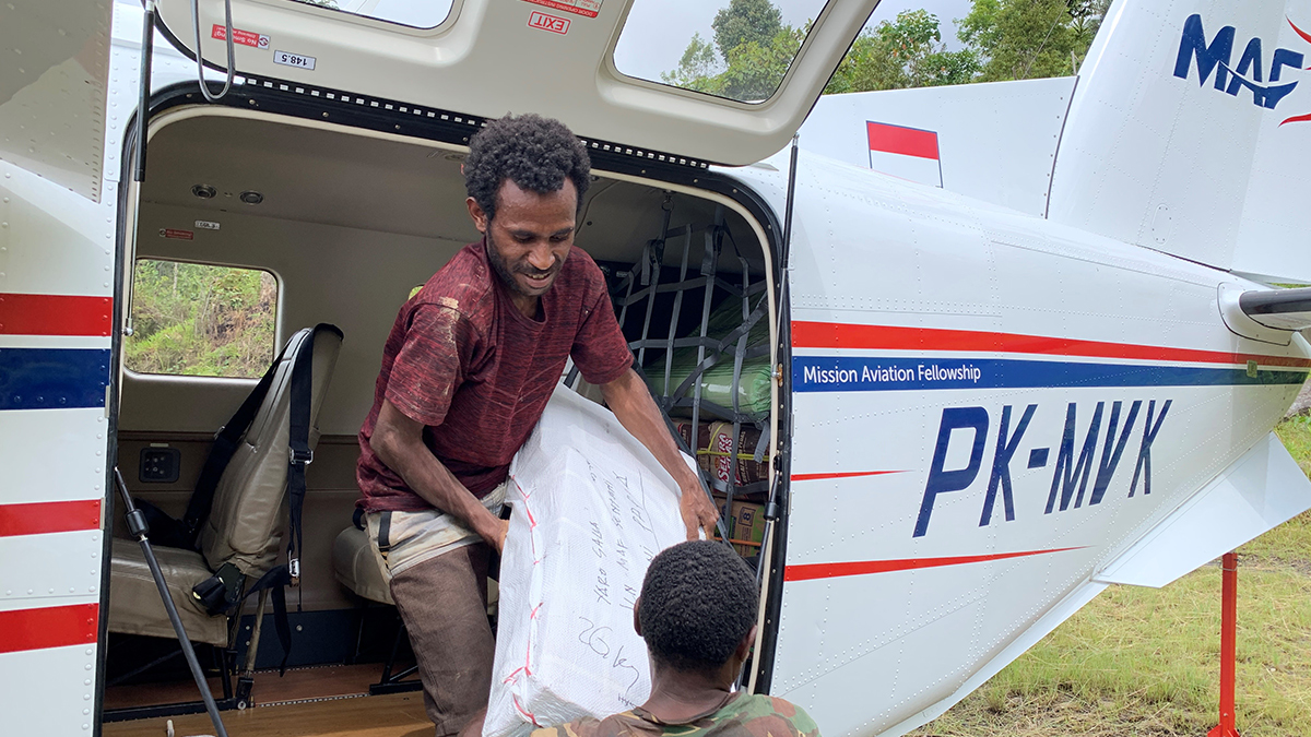 Villagers help offload copies of the New Testament and food supplies delivered by Papua’s latest aircraft, PK-MVK